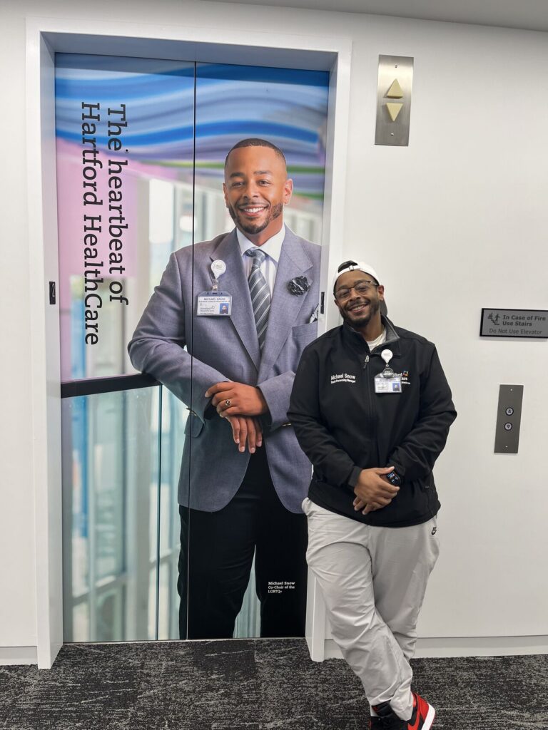 Michael Snow stands next to a picture of himself at Hartford Hospital, where he worked for 20 years. He now works at Orthopedic Associates Surgery Center in Hartford. 